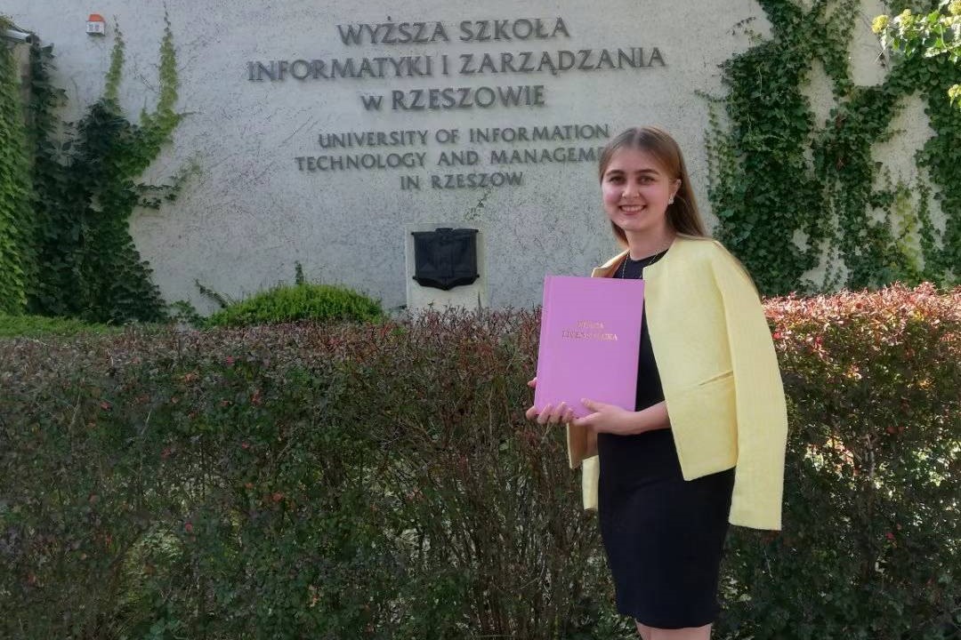 Agnieszka Kąkol z dyplomem WSIiZ przed budynkiem uczelni