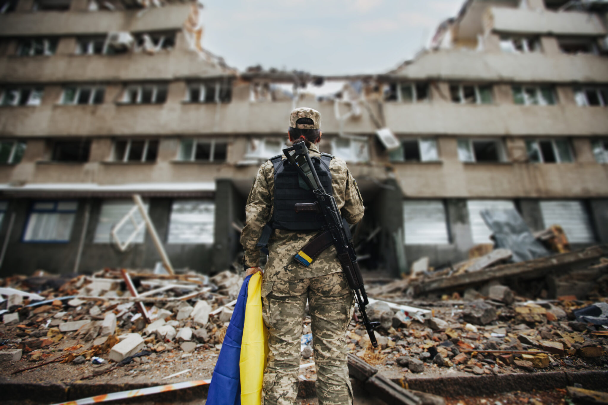 Ukrainian military woman with the Ukrainian flag in her hands on the background of an exploded house