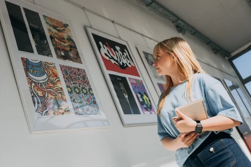 Studentka Grafiki komputerowej i produkcji multimedialnej we WSiIZ w Rzeszowie podziwia prace graficzne na wystawie