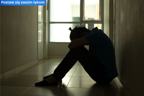Na zdjęciu na podłodze siedzi osoba ze schowaną w rękach twarzą