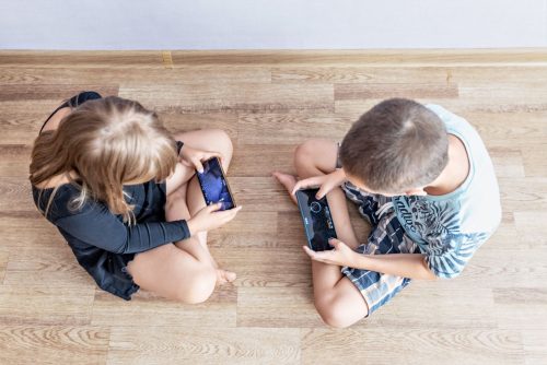 Dwójka dzieci wpatrzona w ekrany telefonów siedzi na podłodze